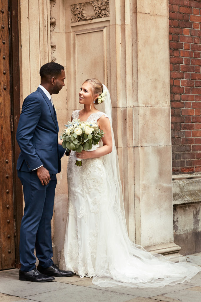 Bride and groom facing each other beside the stone church doorway